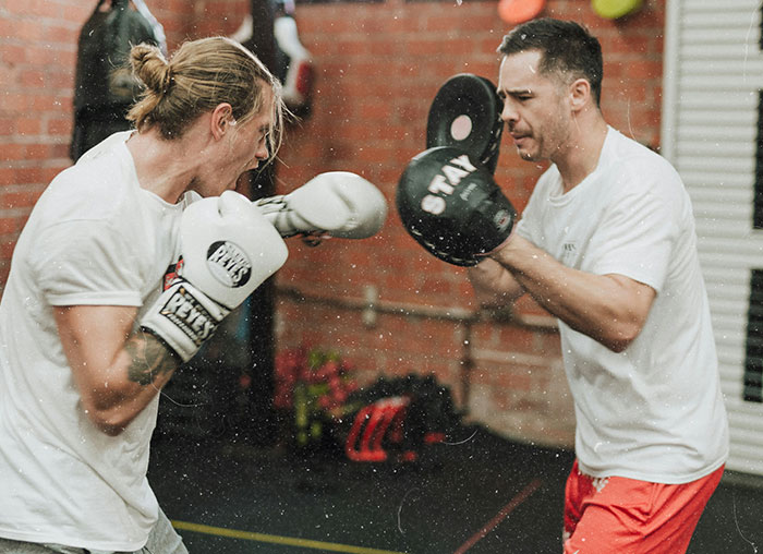 Two men practicing boxing with gloves and pads in a gym, illustrating fake facts people believed from movies.