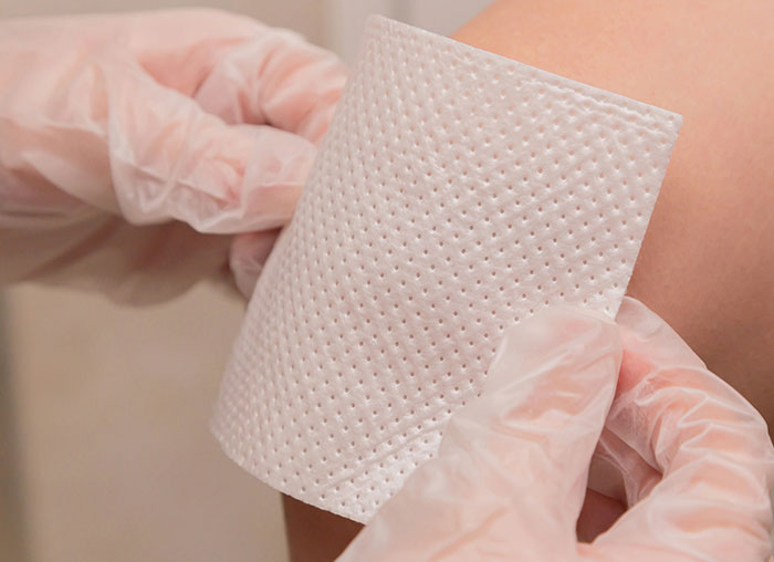 Hands wearing gloves applying a white adhesive bandage to a person's skin for wound care fake facts people believed.