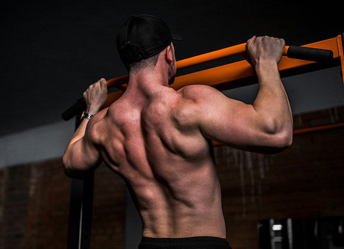Muscular man doing pull-ups on orange bar in gym, illustrating common fake facts people believed from movies.