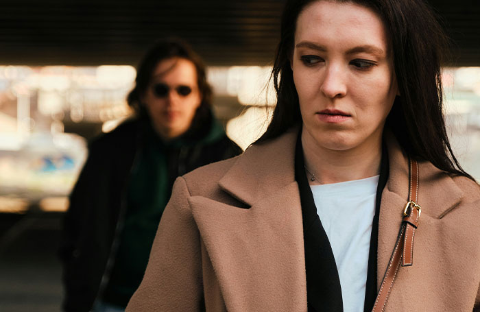 Woman in brown coat looking worried while a man in sunglasses follows from behind, illustrating fake facts from movies.