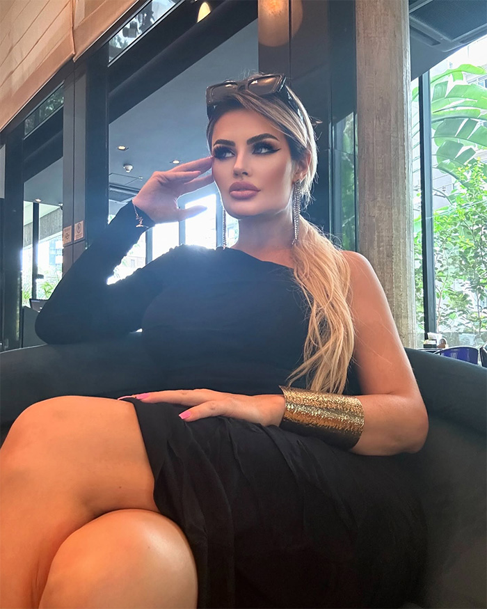 Influencer seated indoors wearing black outfit and gold bracelet, speaking out after Disney World outfit complaints and warning.