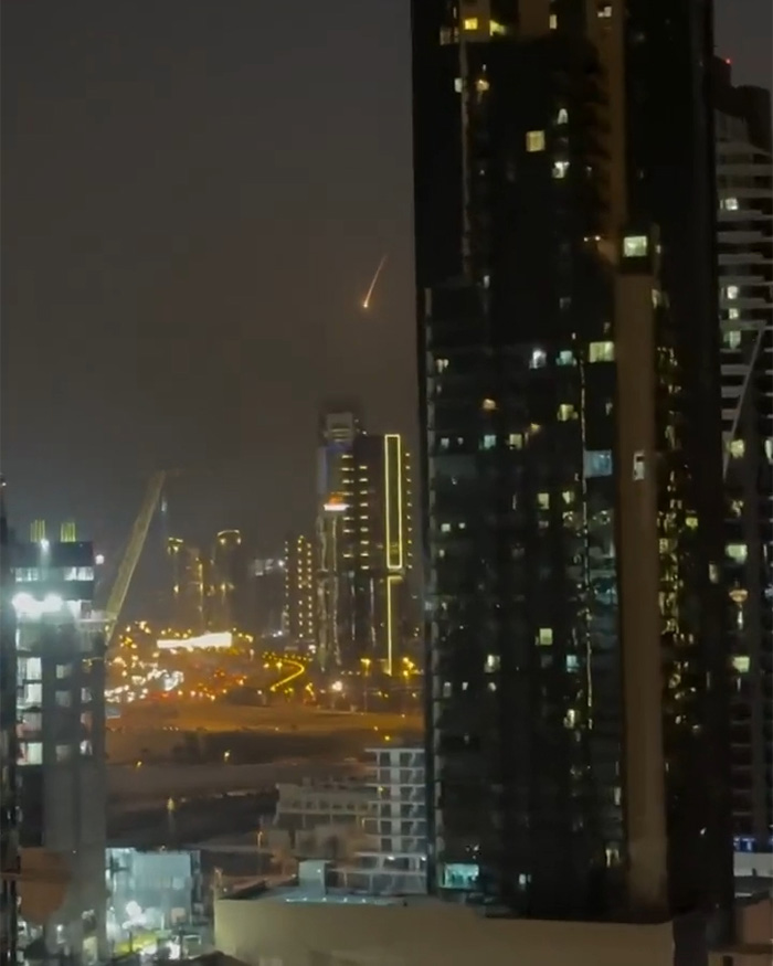 Missile streaks across Dubai night sky amid Iran strikes as city lights glow between towering dark skyscrapers.