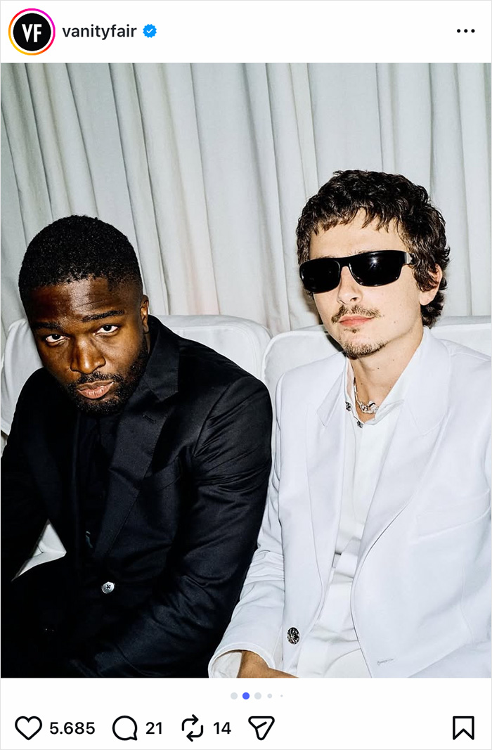 Two men, one in a black suit and the other in a white suit with sunglasses, captured during Oscars night event.