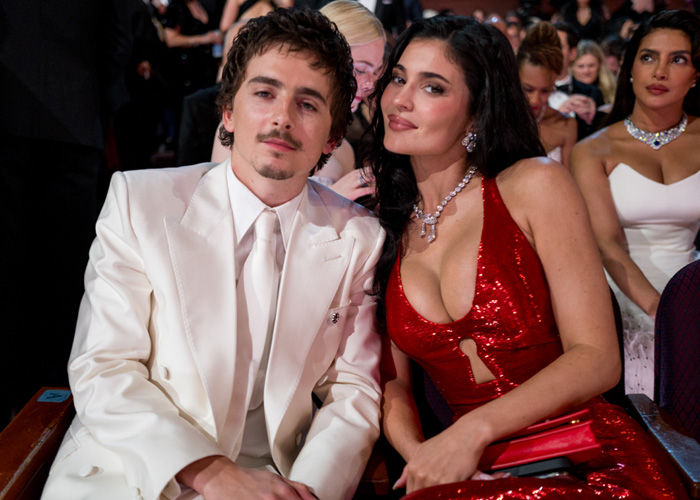 Timoth&eacute;e Chalamet and woman in red dress seated at Oscars event, capturing the awkward and tense atmosphere.