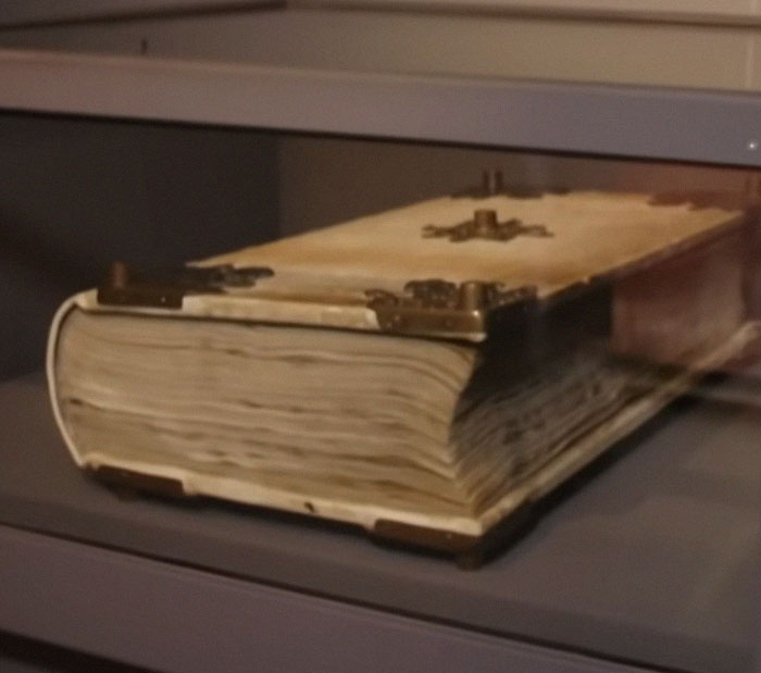 Old aged book with metal corner protectors and clasps displayed in a museum, highlighting strange Earth artifacts.