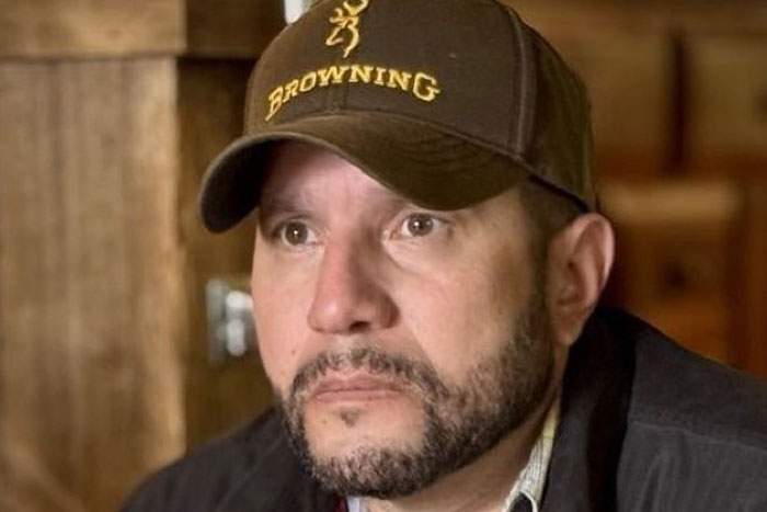 Man wearing a Browning cap with a thoughtful expression, indoors with wooden background, illustrating strange earth concept.