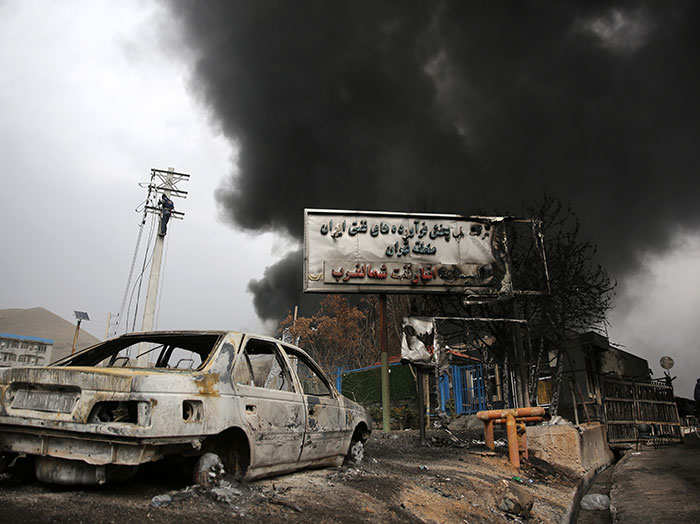 Burned-out car and thick black smoke rising amid war destruction, highlighting influencer stranded claims and refusal to fly economy.