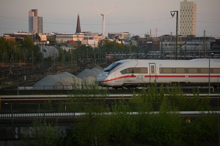 High-speed train passing through an urban area with industrial background, reflecting vanished truths from home countries.