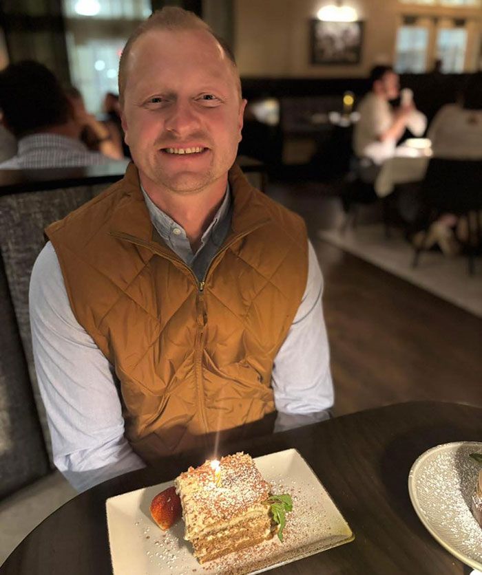 Man in brown vest smiling at a table with dessert, related to heartbreaking high school teacher prank incident details.