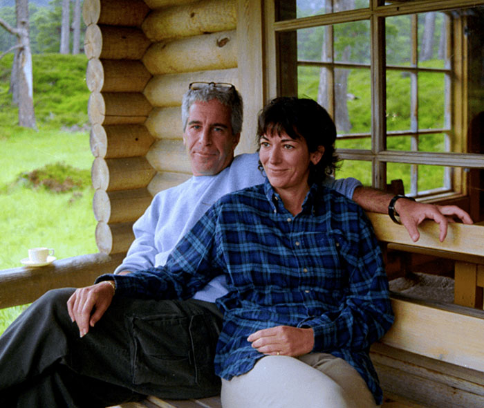 Two people sitting on a wooden bench outside a cabin, highlighting something fishy going on related to Ghislaine Maxwell's prison job.