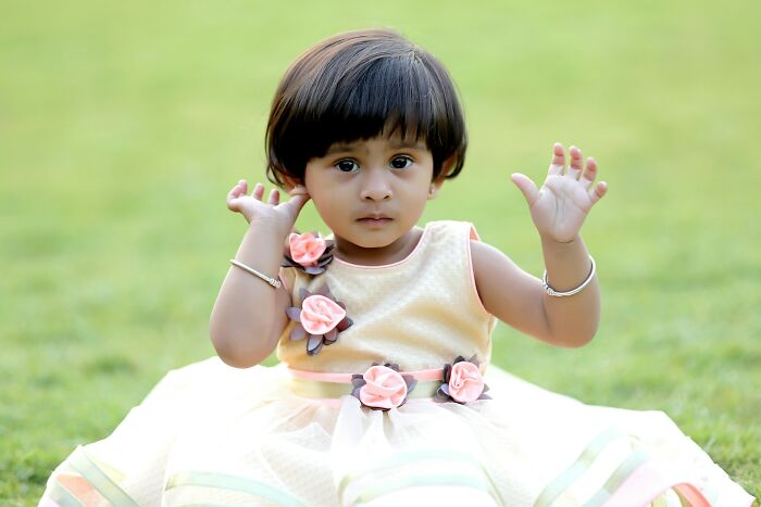 Toddler girl in a cream dress with pink flowers sitting on grass, evoking bizarre encounters that leave people questioning what they saw.