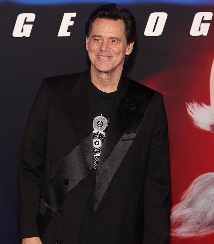 Jim Carrey at an event, wearing a black blazer and shirt, revealing details of the actor’s new face and sadness cause.