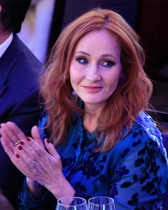 J.K. Rowling wearing a blue patterned dress, clapping and attending an event related to Harry Potter reboot backlash. J.K. Rowling wearing a blue patterned dress, clapping and attending an event related to Harry Potter reboot backlash.