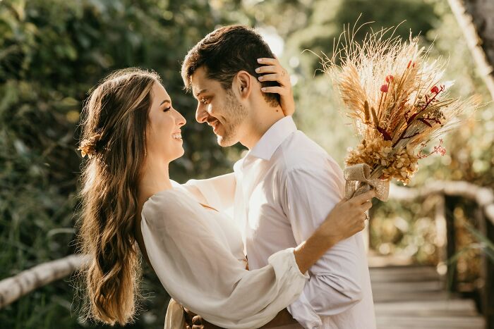 Couple embracing on a wooden bridge surrounded by greenery, illustrating moments before karma hits sabotage attempts.