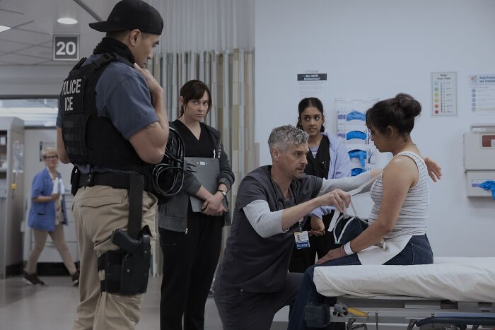 Hospital scene from controversial ICE episode showing police officer, medical staff, and patient in tense interaction. Hospital scene from controversial ICE episode showing police officer, medical staff, and patient in tense interaction.