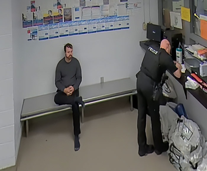 Man sitting on a bench in a holding room while a police officer writes, related to Joseph and Kendra Duggar neighbor news