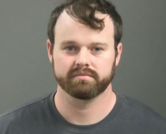 Homem com barba e bigode vestindo camisa escura em ambiente neutro, relacionado à filmagem da prisão da esposa de Joseph Duggar, Kendra.