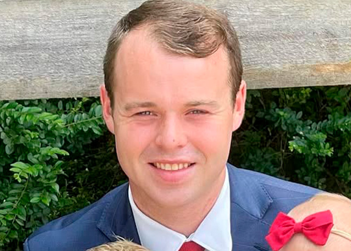 Jovem vestindo terno azul com gravata vermelha sorrindo ao ar livre, relacionado à irmã de Joseph Duggar, Jill, falando após a prisão. Jovem vestindo terno azul com gravata vermelha sorrindo ao ar livre, relacionado à irmã de Joseph Duggar, Jill, falando após a prisão.