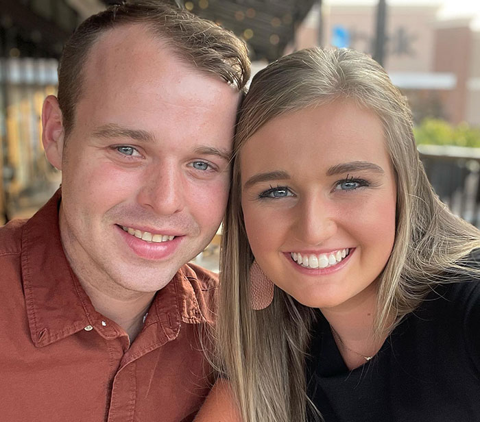 Young couple smiling outdoors, neighbor of Joseph and Kendra Duggar reacting to wife's arrest amid allegations.