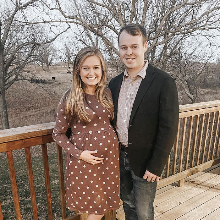 Joseph Garrett Duggar smiling with a woman on a wooden deck outdoors with trees and fields in the background