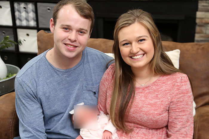 Joseph Garrett Duggar from 19 Kids And Counting smiling with a woman, sitting on a couch in a living room setting.