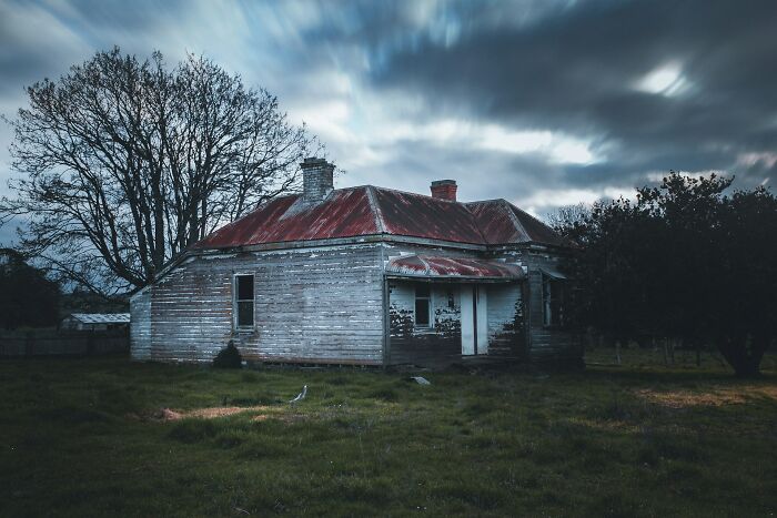 Abandoned house at dusk with dark clouds, evoking terrifying moments that made urban explorers drop their flashlights and run.