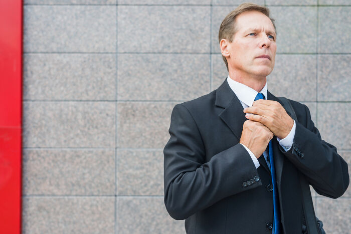 Man in a black suit adjusting tie, reflecting on justice system skepticism and juror experiences outside a courthouse.