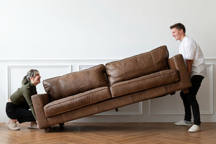 Two people lifting a brown sofa in a bright room symbolizing former jurors reflecting on moments in the jury room.