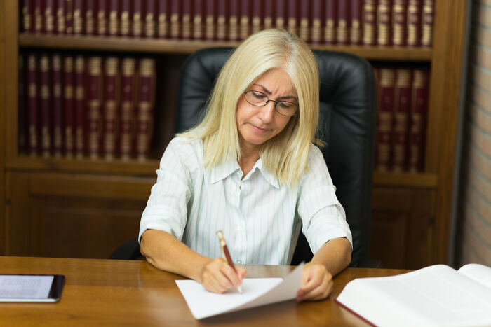 Woman with glasses reviewing legal documents at a desk in a law library, reflecting jury room moments and justice system doubts.