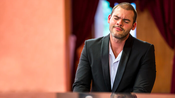 Man in a black suit in a courtroom with eyes closed, reflecting frustration and loss of faith in the justice system.