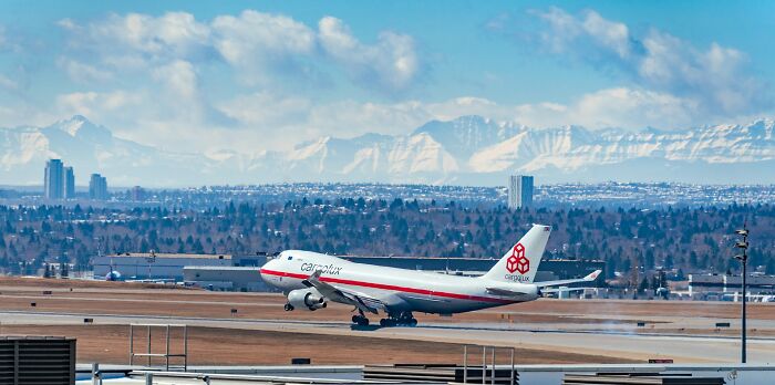 Cargo airplane taking off from airport runway with snowy mountains and city skyline in the background, illustrating scientific facts.