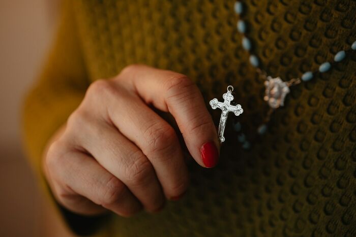 Woman with red nail polish holding a silver cross pendant, symbolizing strength and confidence in shutting down creepy advances.