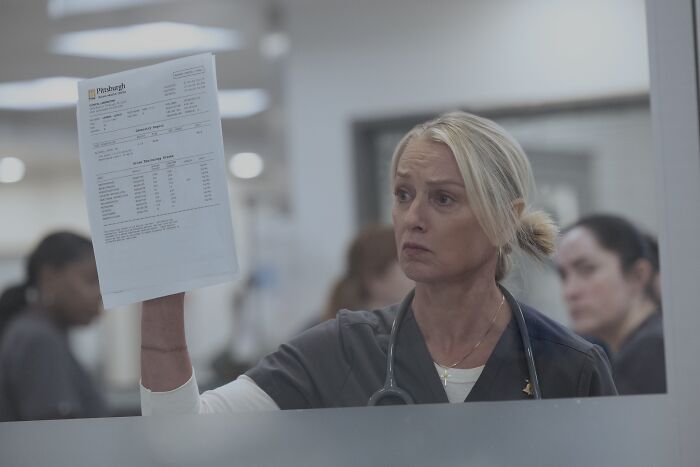 Woman in medical scrubs holding a document, representing a scene from The Pitt Season 2 Episode 13 preview.