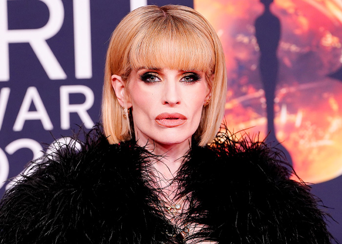 Kelly Osbourne posing at the Brit Awards with bold makeup and a striking black feathered outfit.