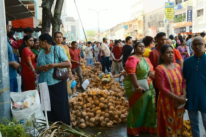 Crowded cultural market scene with people in traditional clothing and a large pile of coconuts on the street.