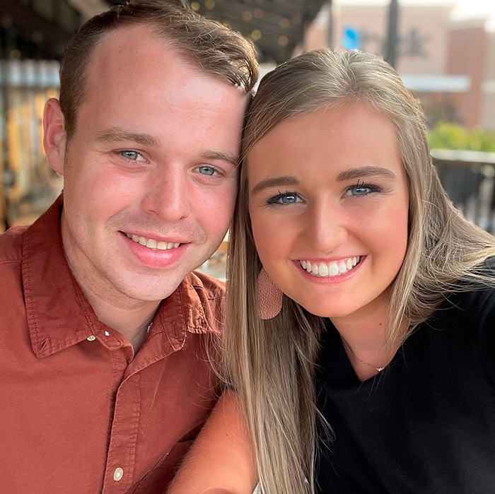 Young couple smiling outdoors, focusing on a close-up portrait with natural lighting and casual attire.