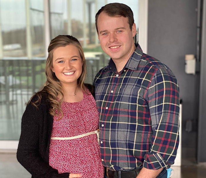 Joseph Duggar e sua esposa Kendra sorrindo juntos dentro de casa, destacando notícias da família Duggar e imagens de prisão.