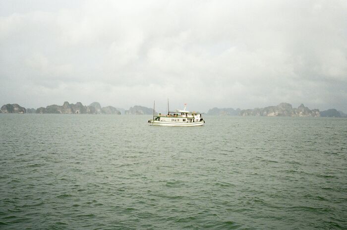 A solitary boat floating on calm sea waters under a cloudy sky with distant rocky islands visible.