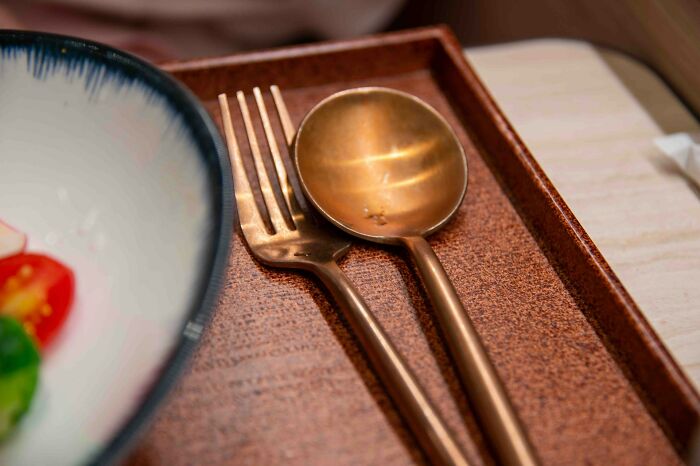 Bronze fork and spoon on a tray next to a bowl, illustrating cultural things people thought were normal until visiting other countries.