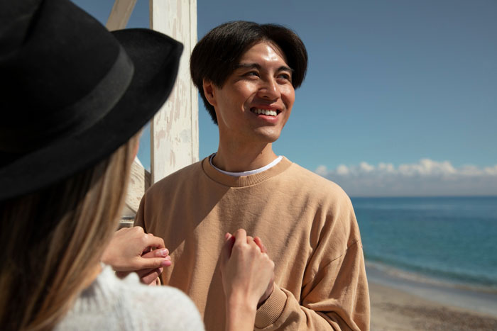 Couple holding hands and smiling on a perfect first date abroad by the beach with clear blue sky.