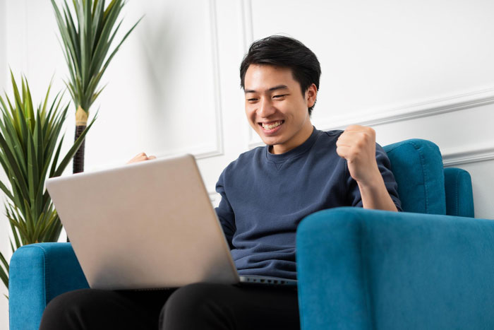 Man happily using laptop in living room, celebrating after perfect first date abroad with no way to reach him.