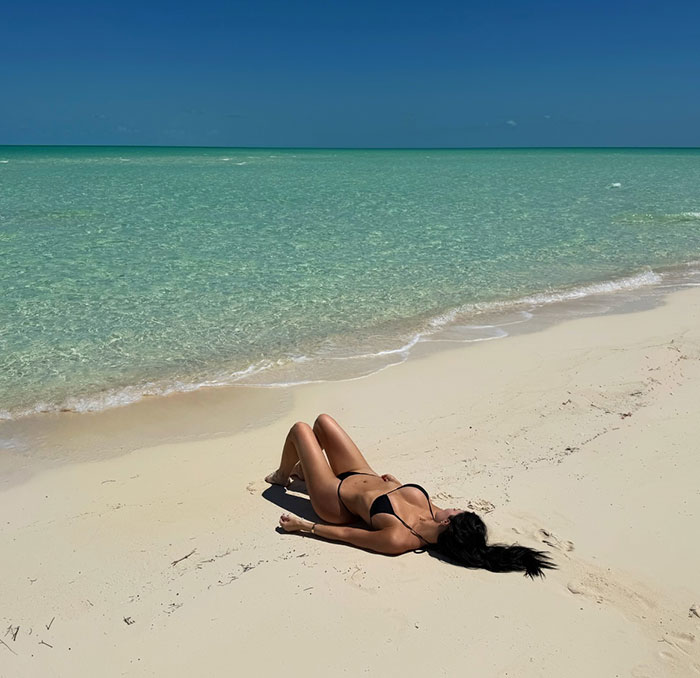 Kylie Jenner lying on a sandy beach in a black bikini, highlighting dramatic differences in personal and public photos.