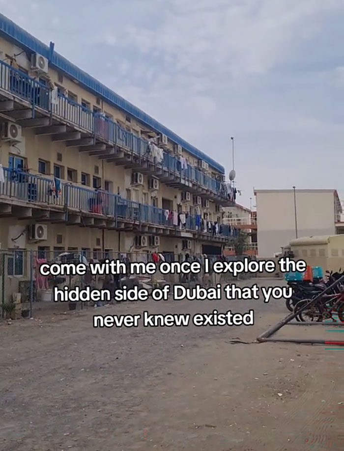 Exterior view of Dubai labor camps with narrow balconies, air conditioners, and scattered bicycles in a dusty environment.