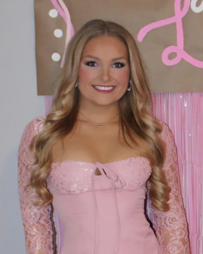 Young woman with long blonde hair wearing a pink lace dress smiling at a celebratory event in Kentucky.