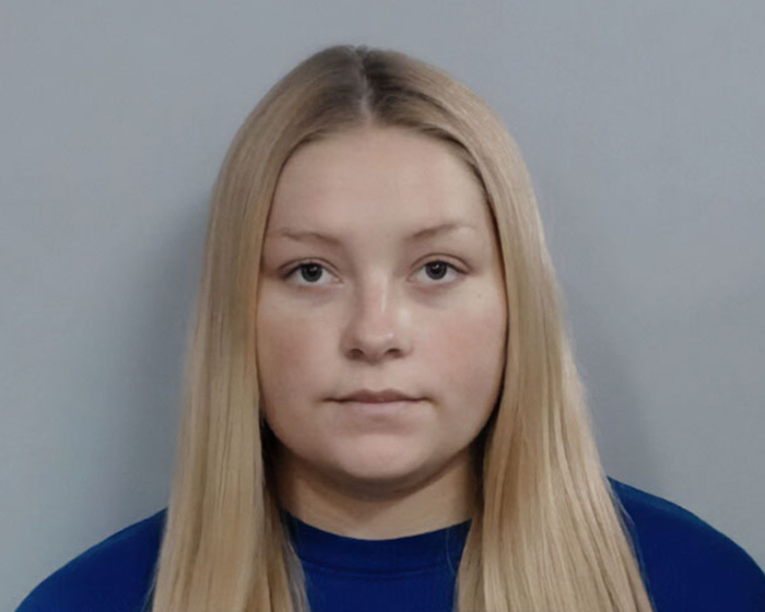Kentucky cheerleader with long blonde hair in a blue shirt, facing the camera in a neutral mugshot style background.