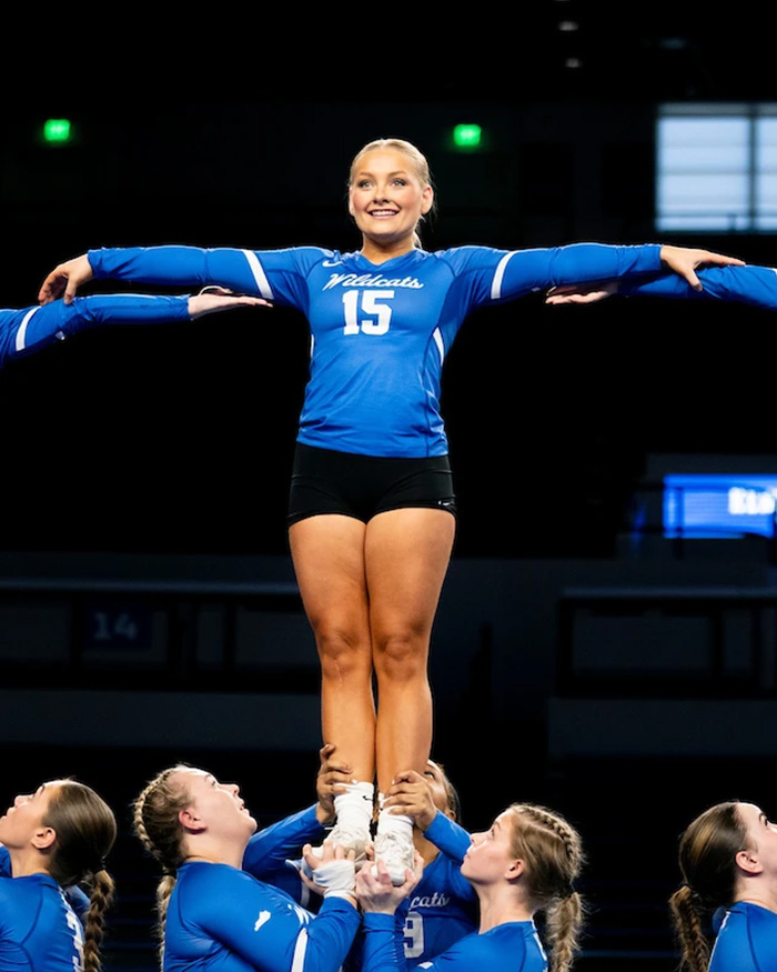 Kentucky cheerleader performing a stunt during a competition with teammates supporting her from below.