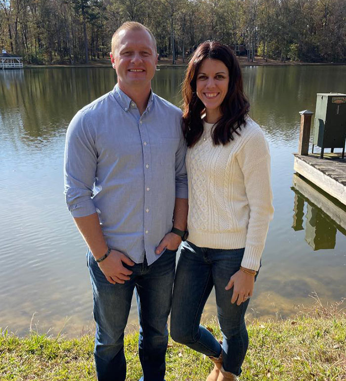 Young couple standing by lakeside in casual clothes, related to Georgia teen charged in teacher's prank incident.