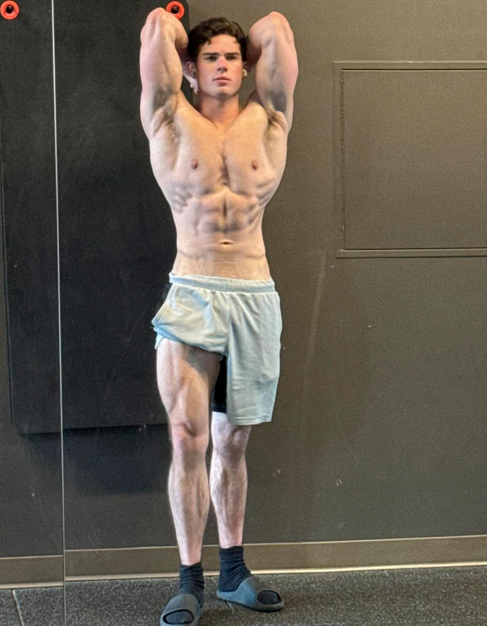 Muscular young man posing shirtless in gym, highlighting looksmaxxing and clavicular features in fitness setting.