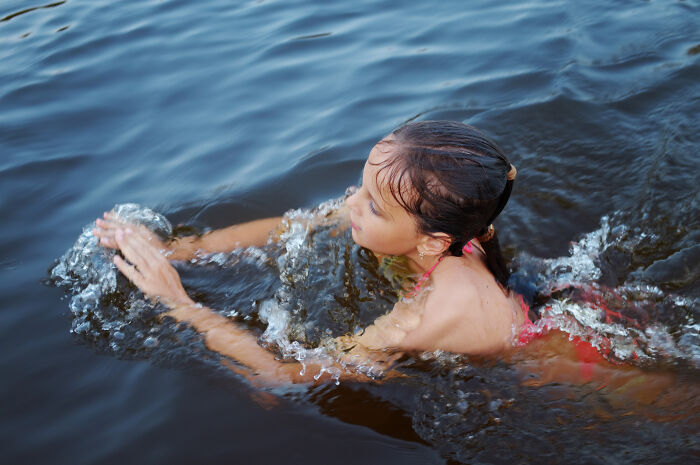 Young girl swimming in a lake with water splashing around her, capturing wholesome moments of dads supporting their kids.