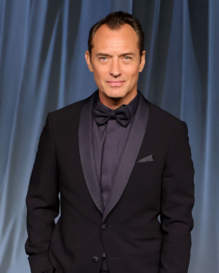 Man in a black tuxedo standing in front of blue curtains, related to Chappell Roan and Jude Law's daughter security guard scandal. Man in a black tuxedo standing in front of blue curtains, related to Chappell Roan and Jude Law's daughter security guard scandal.